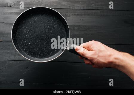 Empty pan in hand on black wood background Stock Photo