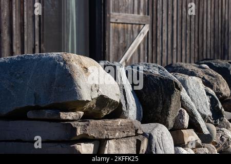 A stone wall sits in front of a wooden barn Stock Photo