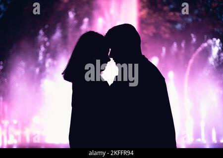 A silhouette of a romantic couple standing together holding each other on blurred purple background Stock Photo