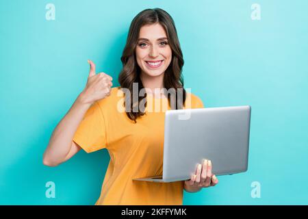 Closeup photo of young pretty nice attractive girl wear yellow t-shirt hold laptop good app facebook developer showing thumb up isolated on cyan color Stock Photo