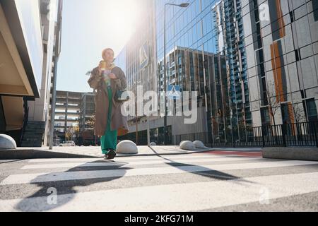 Smiling woman in beige raincoat crosses street at pedestrian crossing Stock Photo