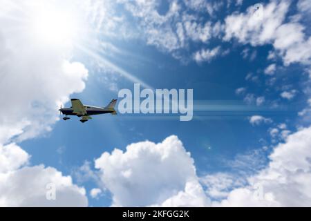 Small private propeller airplane in motion against a beautiful clear blue sky with cumulus clouds and sunbeams. Stock Photo