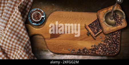 Vintage manual coffee grinder with roasted coffee beans, cup, cutting board and white and brown checkered tablecloth on a wooden table with copy space Stock Photo