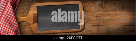 Old wooden cutting board with a blank chalkboard inside, on a wooden table with a red and white checkered tablecloth. Template for recipes or food. Stock Photo