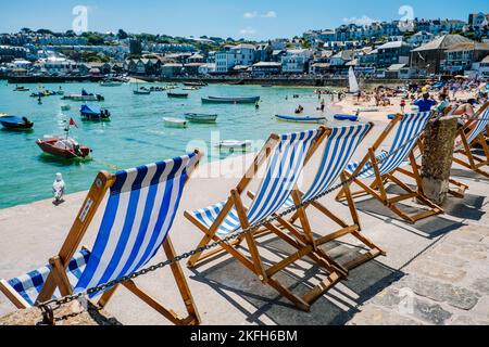 A row of blue and white empty deck chairs overlooking the harbor in bright sunlight Stock Photo