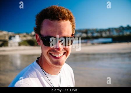 A young Caucasian man wearing sunglasses smiling at the camera on sunny day Stock Photo