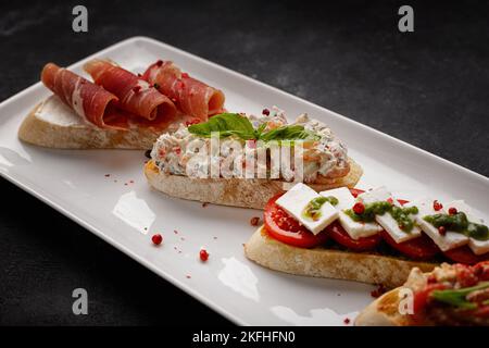 Different bruschetta with jamon, seafood, vegetables and cheese, on dark concrete Stock Photo