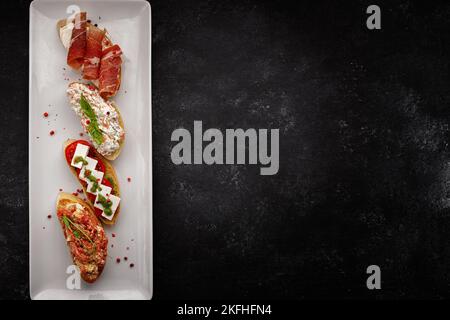 Different bruschetta with jamon, seafood, vegetables and cheese, on dark concrete Stock Photo