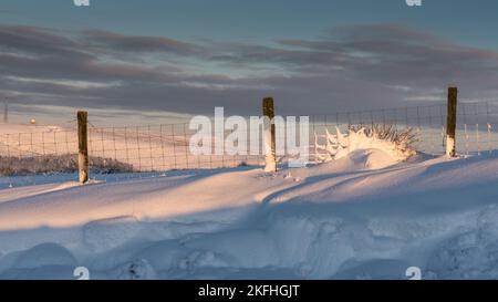 Patterns of a snow star in the fence post. Moody clouds in the sky with hills in the background. Stock Photo