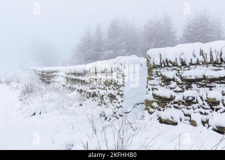 Dry stone wall in the British countryside in Winter, covered in snow. Snow blizzard and wintry landscape with rustic stone wall. Stock Photo