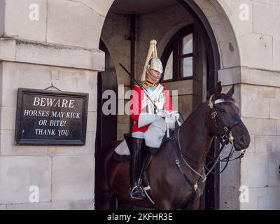 'Beware. Horses may kick or bite' sign beside a mounted Life Guard on duty at the Horse Guards barracks on Whitehall, London, UK. Stock Photo