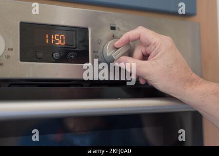 Man setting the timer clock on the oven. Turning knob to set the timer. Cost of living and energy crisis Stock Photo