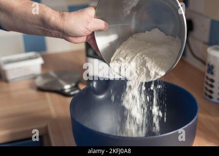 Man pouring flour into a blue mixing bowl. Stock Photo