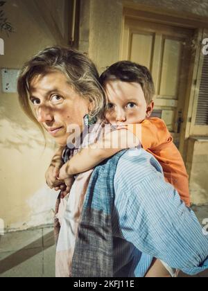 Portrait of caucasian mother piggybacking playful cute son making faces while standing against building Stock Photo