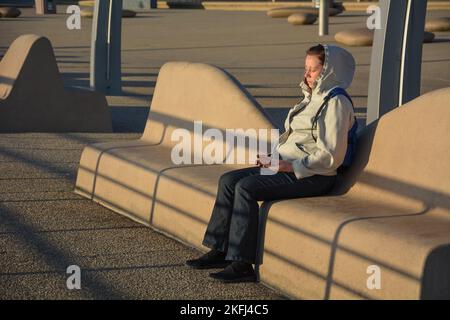 Lady sat on the stone bench on Blackpool promenade, meditating in the warm sunlight. Taken 6 July 2014 on Blackpool seafront. Stock Photo