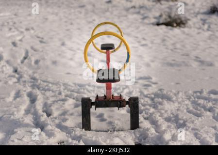 Child's sea saw in the snow covered playground. Bright red and yellow metal frame with black seat. Stock Photo