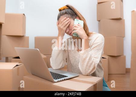 Caucasian woman with headache from moving to new home with laptop and talks to consultant on phone. Stock Photo