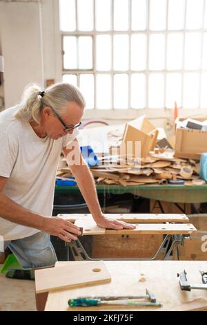 Professional elderly man carpenter artist working on wood using carpentry tools in the workshop Stock Photo