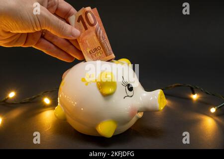 Putting ten euro banknote in a piggy bank, on a dark background with led lights. Side view. The christmas concept of saving money. copy space. Stock Photo