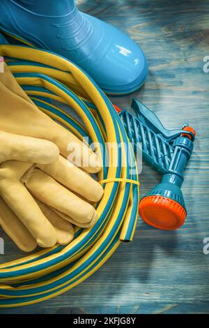 Rubber waterproof boots leather protective gloves garden hose on wooden board gardening concept. Stock Photo