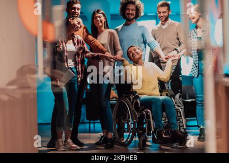 Businesswoman in a wheelchair on break in a modern office with her team in the background Stock Photo