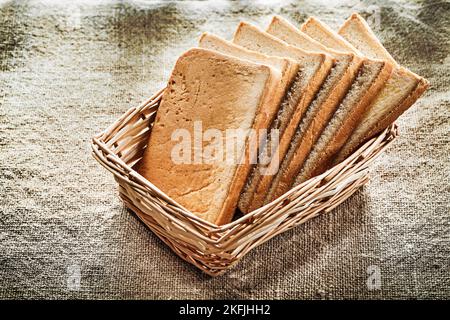 Wicker basket sliced bread on vintage burlap background. Stock Photo