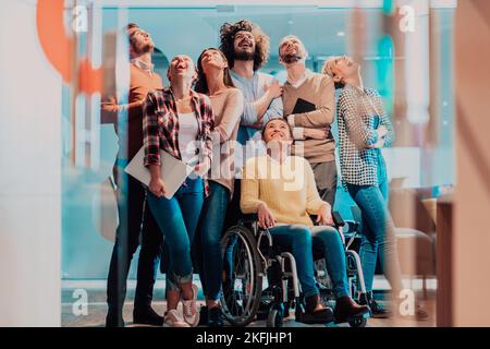 Businesswoman in a wheelchair on break in a modern office with her team in the background Stock Photo