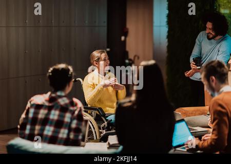 Businesswoman in wheelchair having business meeting with team at modern office. A group of young freelancers agree on new online business projects Stock Photo