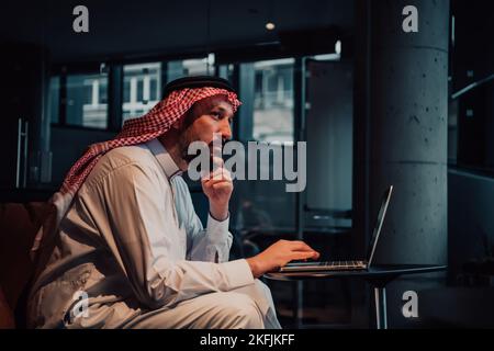 An elderly Arab man sitting in the office and analyzes data on his laptop Stock Photo