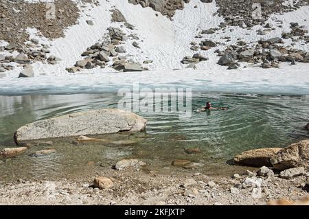 man swimming in cold mountain lake with snow in it Stock Photo