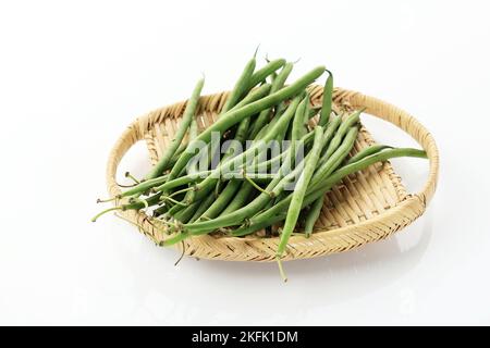 Pile of Raw Green Baby Fine Beans on a Rattan Tray Plate above Isolated White Background Stock Photo