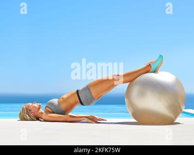 Shes in the zone. an attractive young woman working out with an exercise ball by a swimming pool. Stock Photo