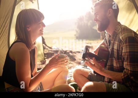Enjoying a forest getaway. a young man playing guitar to his girlfriend in a tent. Stock Photo