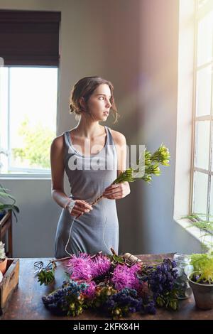 Dont quit your daydream. a beautiful woman completing a floral bouquet on a wooden counter top. Stock Photo