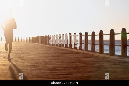 Its all about endurance. A young woman running along the promenade at sunset. Stock Photo