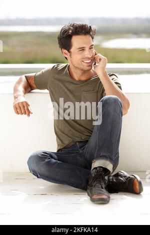 Making a call outside. A handsome young man sitting outside and making a call. Stock Photo