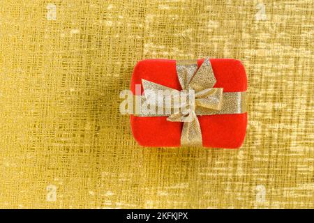 Top view of a giftbox wrapped in red and tied up with a golden ribbon and bow isolated on a golden background. Stock Photo