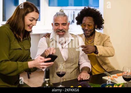 happy friends looking at the smart phone for cooking vegan food, focus on bearded man, preparing vegetarian dinner, cooking using technology on line, Stock Photo