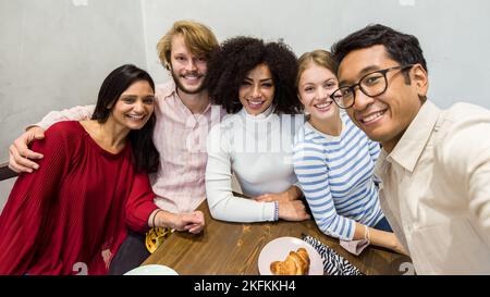 smiling friends taking a selfie during breakfast, multiracial university Erasmus group in a moment of relaxation, coffee shop activities with young st Stock Photo