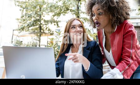 business women working outdoor in remote with laptop, focus on red head professional woman pointing at a document on screen device Stock Photo