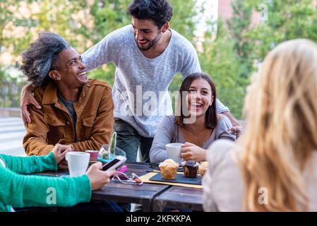 group of friends having fun during breakfast, people of different ethnic groups at the table of a pastry bar, students on break drinking coffee and ca Stock Photo