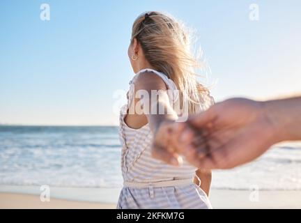 Hands, love and walking with a couple on the beach during summer vacation for romance or bonding. Sea, travel and holding hands with a woman leading Stock Photo