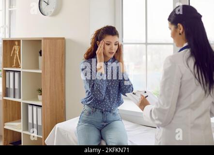 Young Caucasian woman at doctor appointment holding head complaining of headache or migraine Stock Photo
