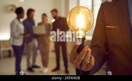 Man holding idea lightbulb in hand, with creative business team working in background Stock Photo
