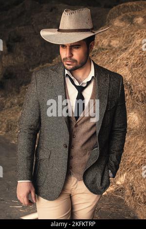 A male wearing suit and cowboy hat standing near haycock Stock Photo