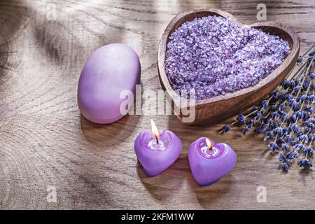 Composition of candles wooden spoon sea salt scented lavender piece of soap on wood board spa treatment concept. Stock Photo