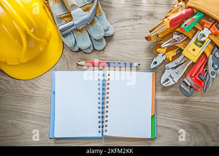 Construction tooling tool belt protective gloves claw hammer notepad pencil hard hat. Stock Photo