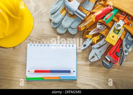 Construction tooling tool belt safety gloves claw hammer notepad pencil hard hat. Stock Photo