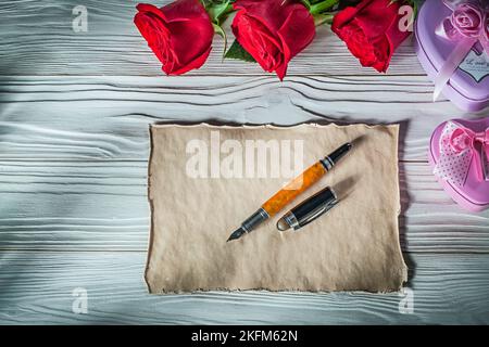 Heart-shaped metal gift boxes red roses vintage paper fountain pen on wooden board celebrations concept. Stock Photo