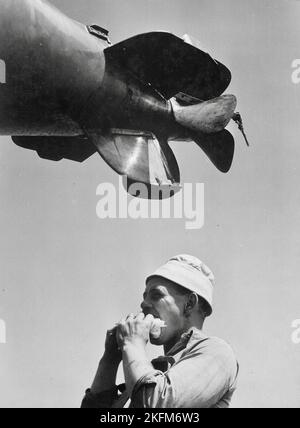 Charles Fenno Jacobs - Sailor eating sandwich beneath propellers of torpedo being loaded aboard U.S. submarine at New London, Connecticut, USA - 1943 Stock Photo